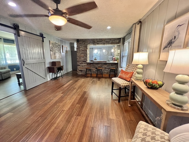 living room featuring a barn door, ceiling fan, dark hardwood / wood-style floors, and a textured ceiling