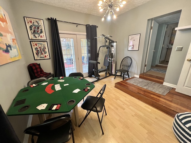 game room featuring french doors, a textured ceiling, a chandelier, and light hardwood / wood-style floors