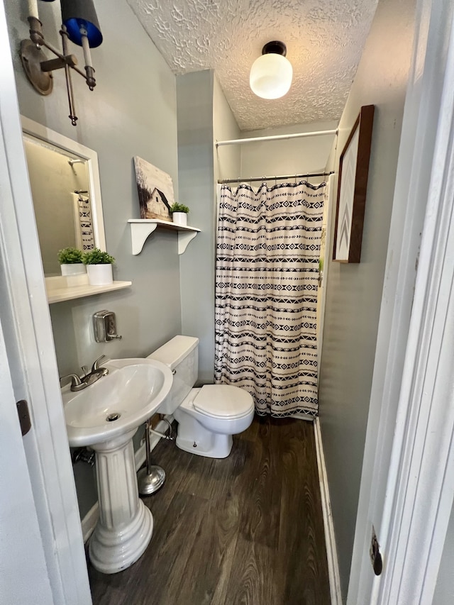 bathroom with curtained shower, wood-type flooring, toilet, and a textured ceiling