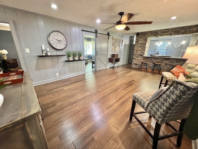 living room featuring a textured ceiling, wood-type flooring, ceiling fan, and a barn door