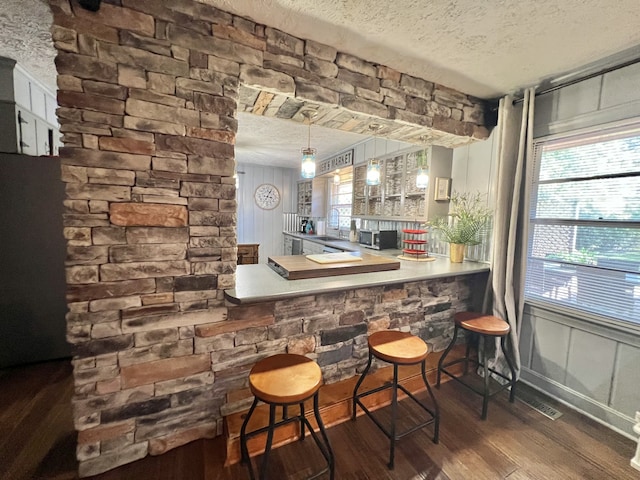 bar with a textured ceiling, dark hardwood / wood-style flooring, decorative light fixtures, and sink