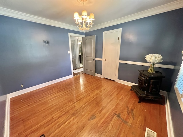 interior space featuring a wood stove, crown molding, an inviting chandelier, and hardwood / wood-style floors