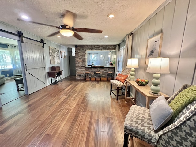 living room featuring a textured ceiling, a barn door, ceiling fan, and hardwood / wood-style flooring