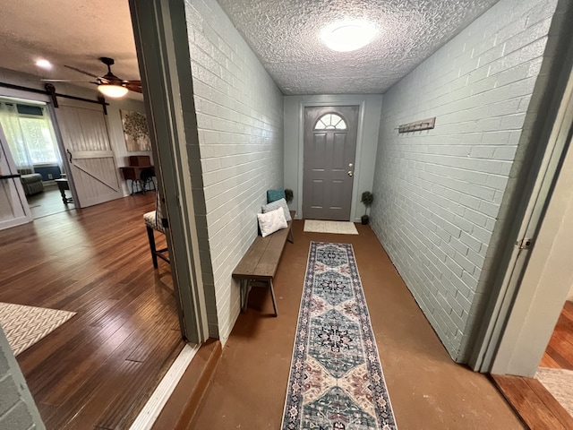 doorway featuring a textured ceiling, brick wall, hardwood / wood-style flooring, a barn door, and ceiling fan