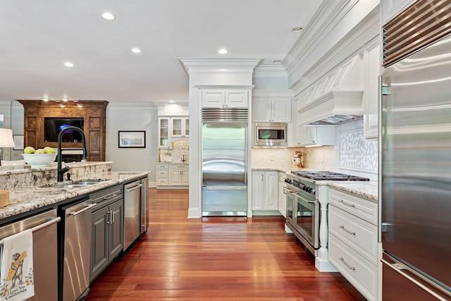 kitchen with crown molding, white cabinetry, built in appliances, light stone countertops, and dark wood-type flooring