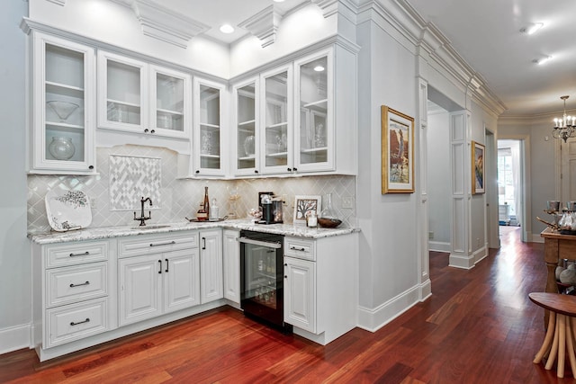 bar with wine cooler, an inviting chandelier, crown molding, dark wood-type flooring, and white cabinetry