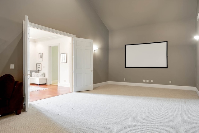 carpeted home theater with ornamental molding and vaulted ceiling