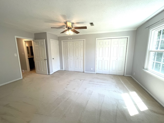 unfurnished bedroom with a textured ceiling, light colored carpet, ceiling fan, and multiple closets