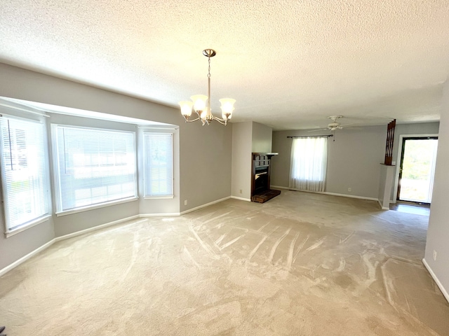 unfurnished living room featuring a textured ceiling, carpet, and ceiling fan with notable chandelier