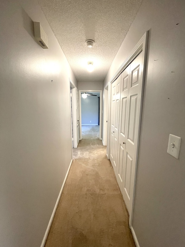 corridor with light colored carpet and a textured ceiling