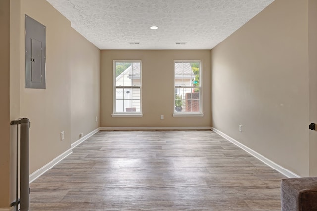 spare room with electric panel, a textured ceiling, and light wood-type flooring