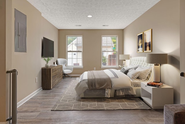 bedroom with a textured ceiling, electric panel, and light hardwood / wood-style floors