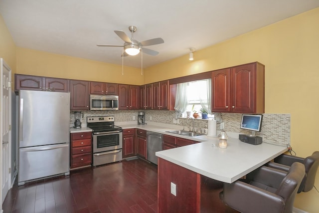 kitchen featuring kitchen peninsula, sink, dark wood-type flooring, appliances with stainless steel finishes, and a breakfast bar area