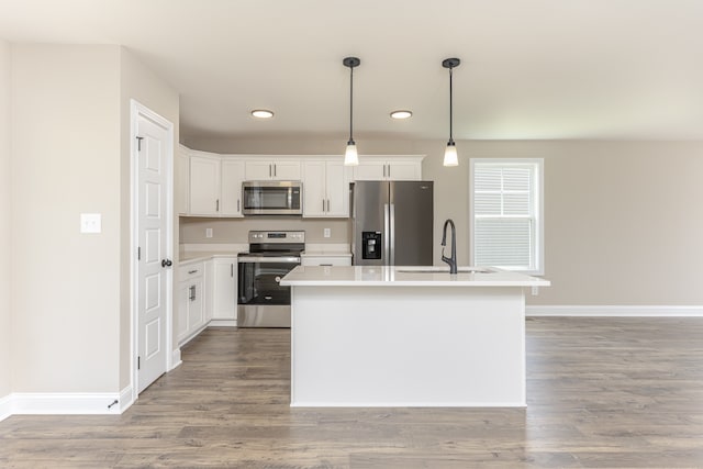 kitchen featuring white cabinets, hanging light fixtures, hardwood / wood-style floors, appliances with stainless steel finishes, and an island with sink