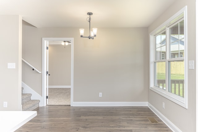 unfurnished dining area featuring a healthy amount of sunlight, a notable chandelier, and dark hardwood / wood-style floors