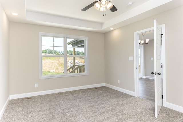 carpeted spare room with ceiling fan with notable chandelier and a tray ceiling