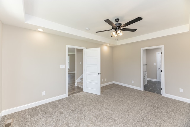 unfurnished bedroom with a tray ceiling, ensuite bath, ceiling fan, and carpet floors