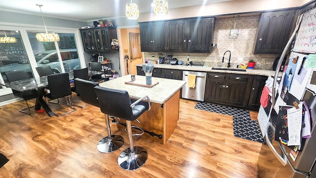 kitchen with sink, appliances with stainless steel finishes, ornamental molding, a kitchen island, and decorative light fixtures