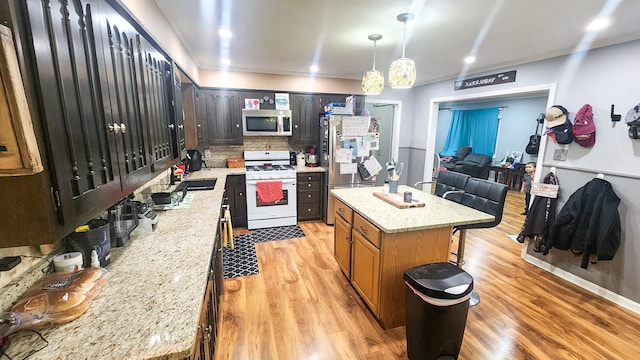 kitchen with sink, decorative light fixtures, stainless steel appliances, light stone countertops, and a kitchen island with sink