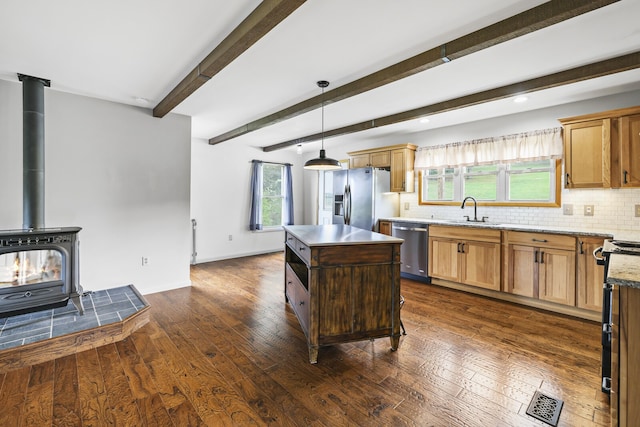 kitchen with a wood stove, a kitchen island, dark wood-type flooring, hanging light fixtures, and appliances with stainless steel finishes