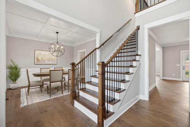 stairway with hardwood / wood-style floors, crown molding, and a notable chandelier