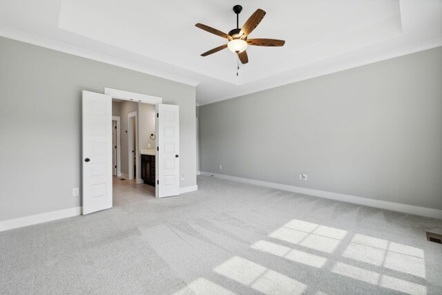 unfurnished bedroom featuring light carpet, ornamental molding, ceiling fan, a raised ceiling, and ensuite bathroom