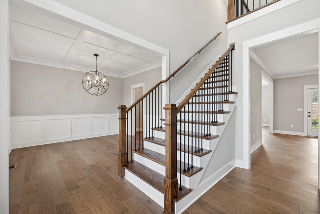 staircase with ornamental molding, an inviting chandelier, and wood-type flooring