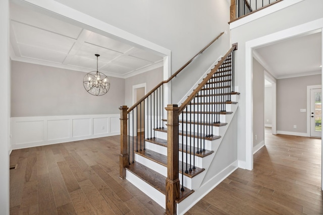 stairway featuring a notable chandelier, wood-type flooring, coffered ceiling, and ornamental molding