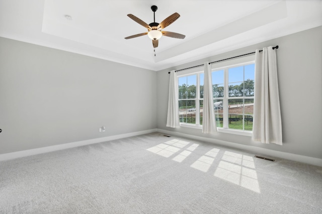 carpeted empty room featuring baseboards, a raised ceiling, visible vents, and a ceiling fan