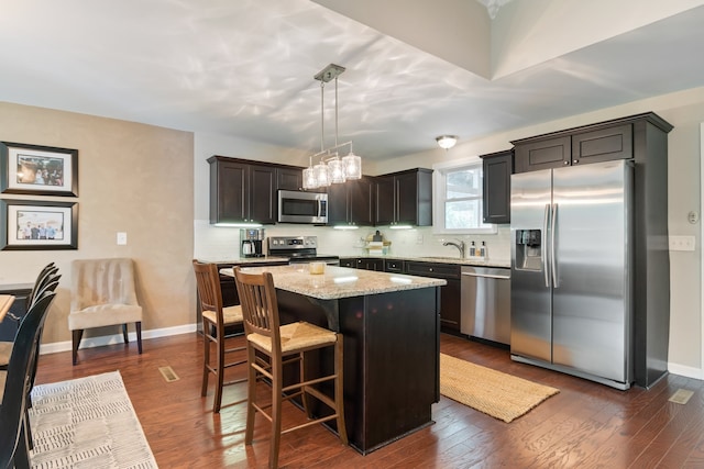 kitchen featuring hanging light fixtures, appliances with stainless steel finishes, light stone countertops, dark hardwood / wood-style floors, and a kitchen island