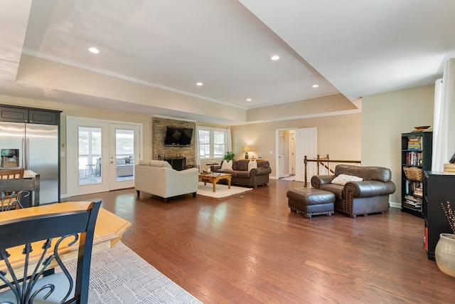 living room featuring french doors, dark hardwood / wood-style floors, crown molding, and a stone fireplace