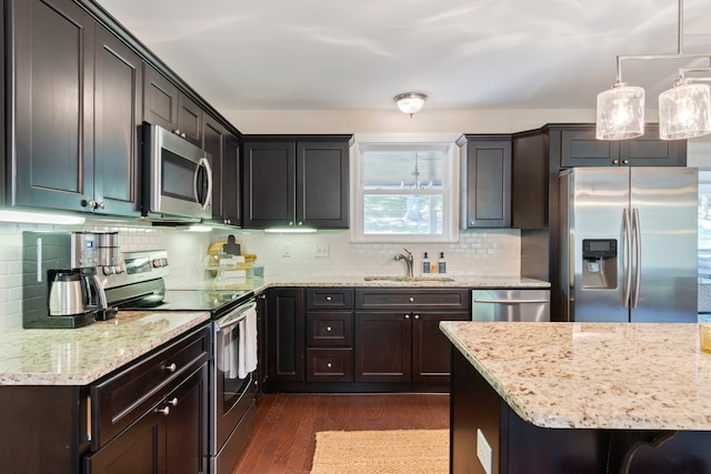 kitchen featuring decorative light fixtures, appliances with stainless steel finishes, light stone countertops, sink, and dark wood-type flooring