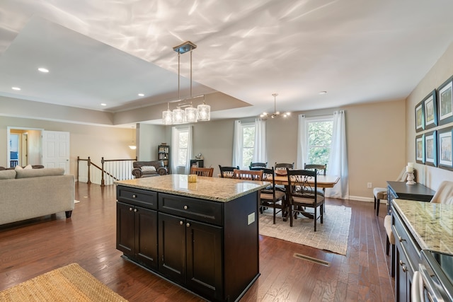 kitchen with dark hardwood / wood-style flooring, a center island, hanging light fixtures, stainless steel range oven, and light stone counters