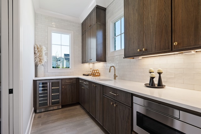 kitchen with beverage cooler, light hardwood / wood-style flooring, dark brown cabinets, and sink