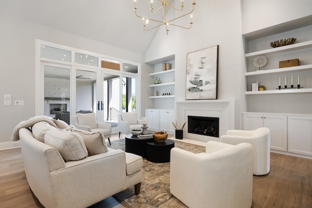 living room featuring high vaulted ceiling, hardwood / wood-style floors, built in shelves, and a notable chandelier