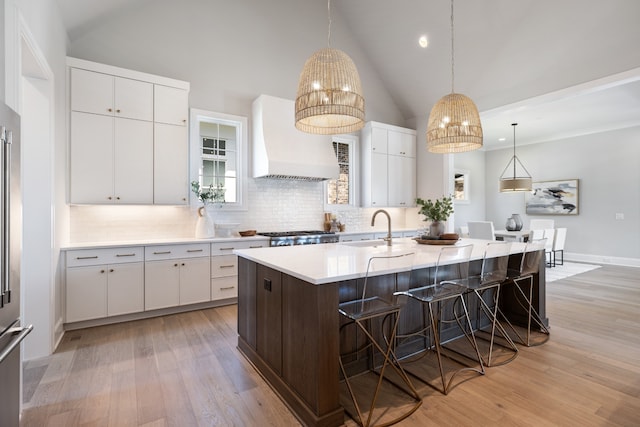 kitchen featuring custom exhaust hood, light wood-type flooring, white cabinetry, and a kitchen island with sink