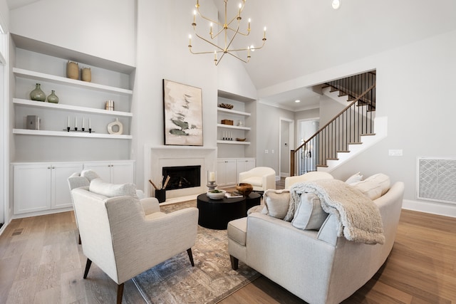 living room with a fireplace, light wood-type flooring, built in shelves, a chandelier, and high vaulted ceiling