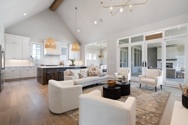 living room with a fireplace, beamed ceiling, high vaulted ceiling, a chandelier, and light hardwood / wood-style flooring