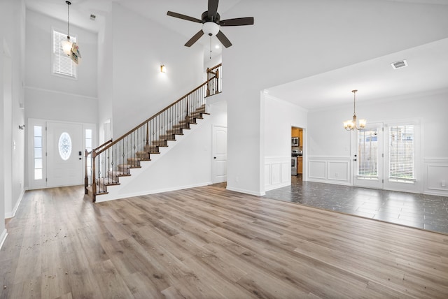 unfurnished living room with crown molding, a high ceiling, hardwood / wood-style floors, and ceiling fan with notable chandelier