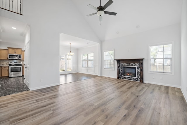 unfurnished living room with high vaulted ceiling, ceiling fan with notable chandelier, a fireplace, and wood-type flooring