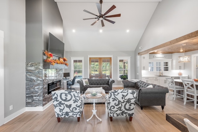 living room featuring a premium fireplace, light hardwood / wood-style floors, sink, high vaulted ceiling, and ceiling fan