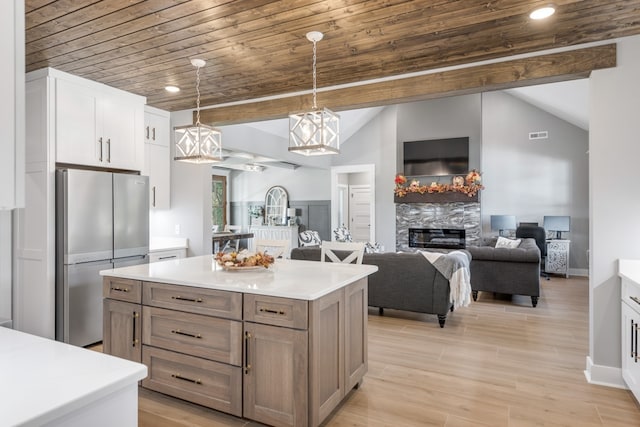 kitchen featuring stainless steel fridge, white cabinetry, decorative light fixtures, a center island, and vaulted ceiling