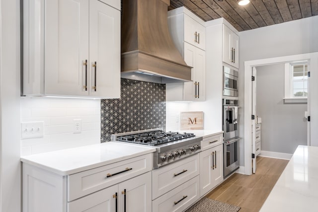 kitchen with backsplash, premium range hood, light hardwood / wood-style floors, stainless steel appliances, and white cabinets