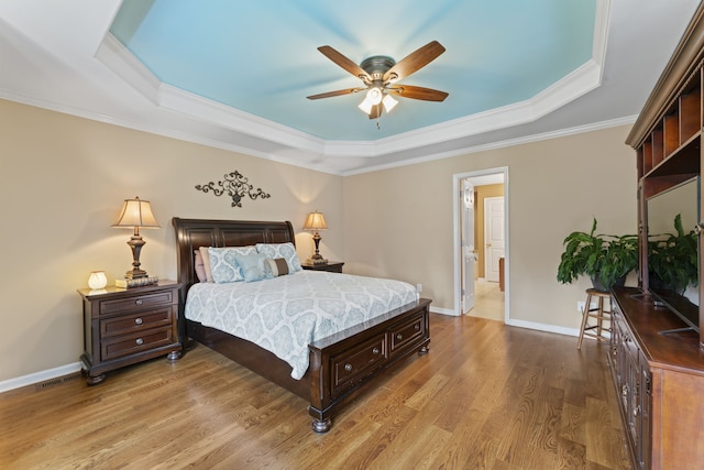 bedroom with a tray ceiling, crown molding, wood-type flooring, and ceiling fan