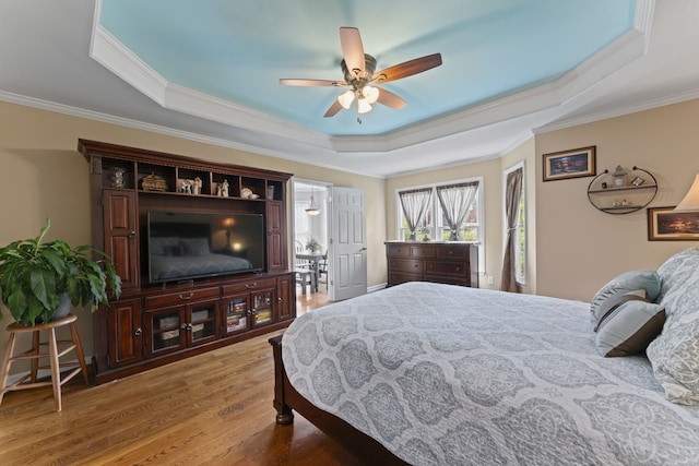 bedroom featuring a tray ceiling, wood-type flooring, ornamental molding, and ceiling fan