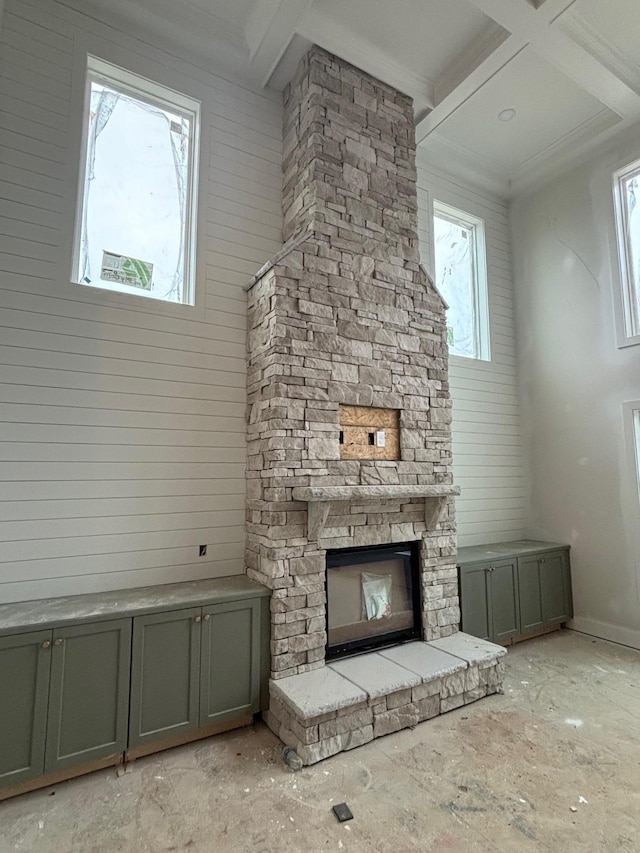 unfurnished living room featuring beam ceiling, a stone fireplace, a wealth of natural light, and coffered ceiling