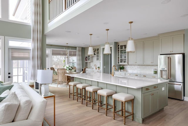 kitchen featuring high quality fridge, sink, a large island with sink, hanging light fixtures, and light hardwood / wood-style floors