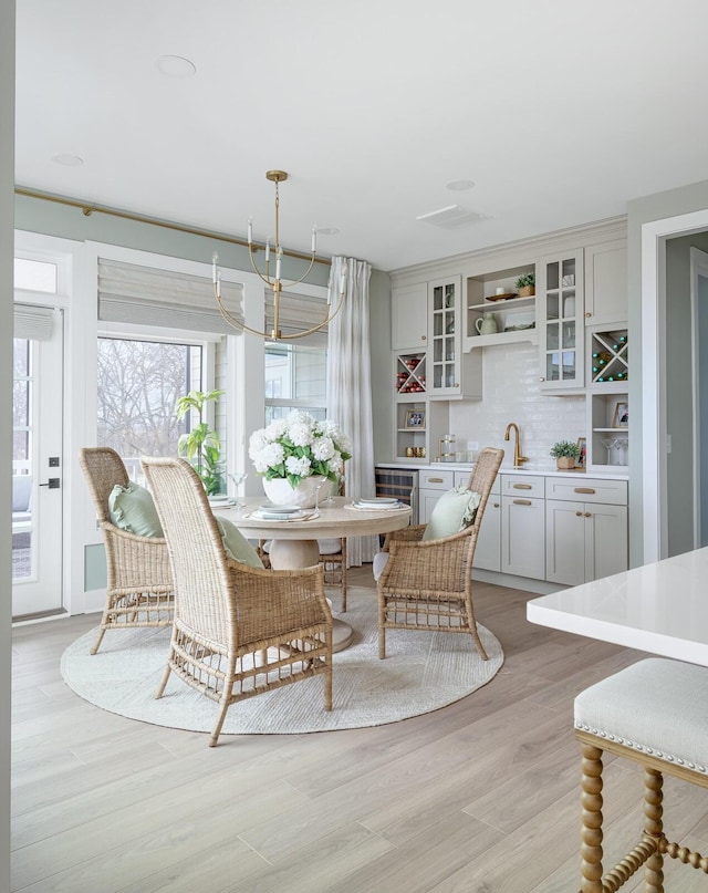 dining room with bar area, light hardwood / wood-style floors, and a notable chandelier