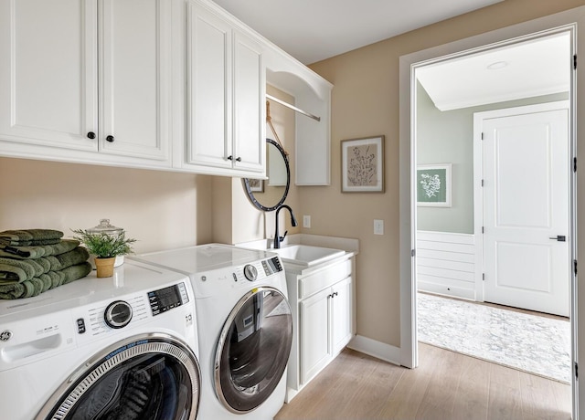 clothes washing area featuring cabinets, sink, washing machine and clothes dryer, and light wood-type flooring