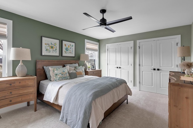 bedroom featuring multiple closets, light colored carpet, and ceiling fan